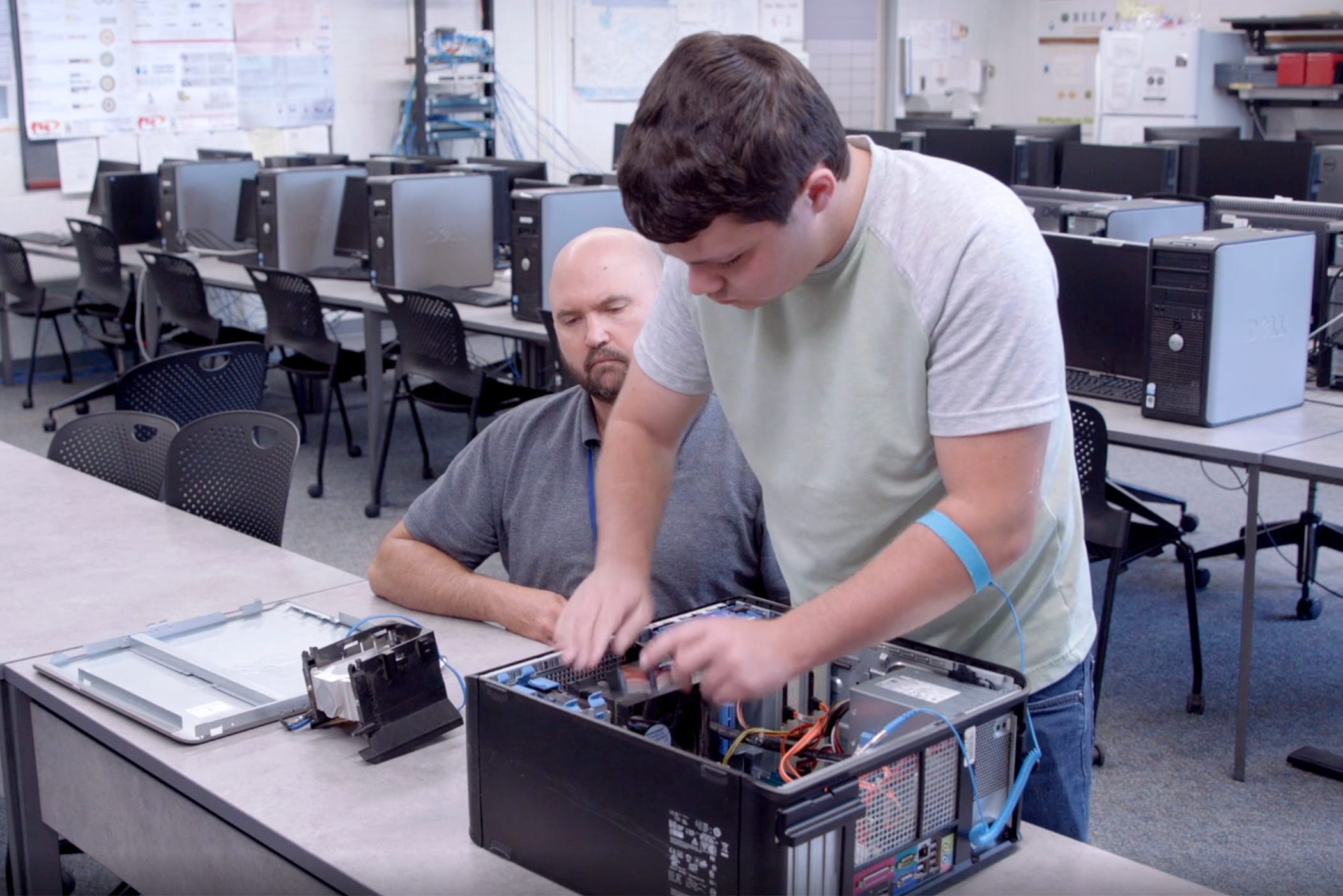 IT Instructor overseeing student re-assemble the interworkings of a computer